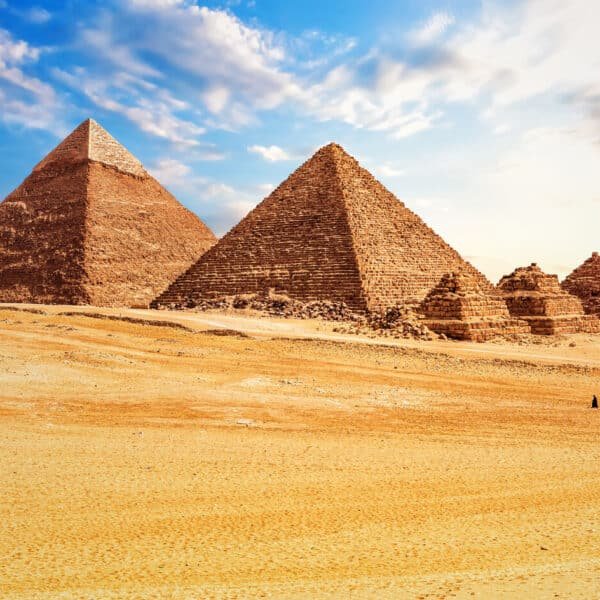 Turistas montando camellos frente a la pirámide de Menkaure en Egipto.