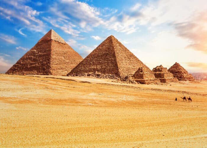 Turistas montando camellos frente a la pirámide de Menkaure en Egipto.