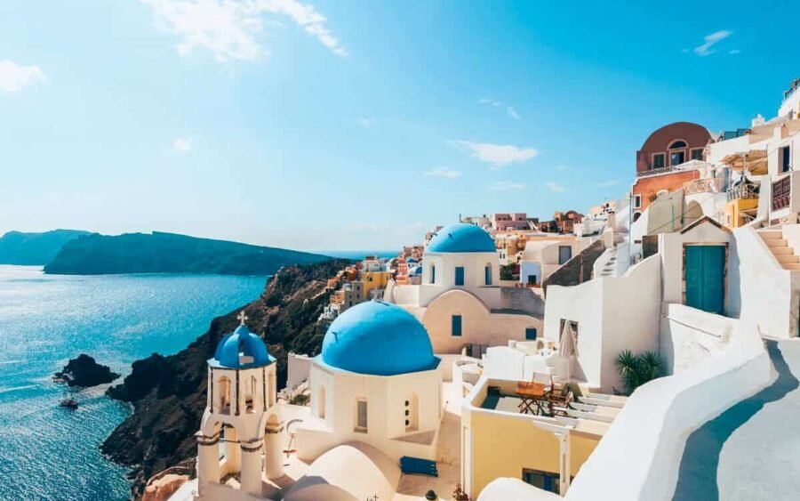 Vista panorámica de una ciudad costera en Grecia con casas blancas y mar azul.