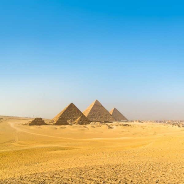 Vista panorámica de las tres pirámides de Giza bajo un cielo azul claro.