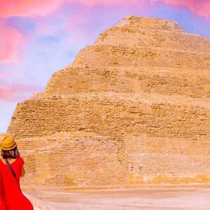 Turista con vestido rojo frente a la pirámide de Zoser al atardecer.