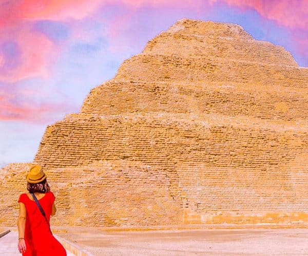 Turista con vestido rojo frente a la pirámide de Zoser al atardecer.
