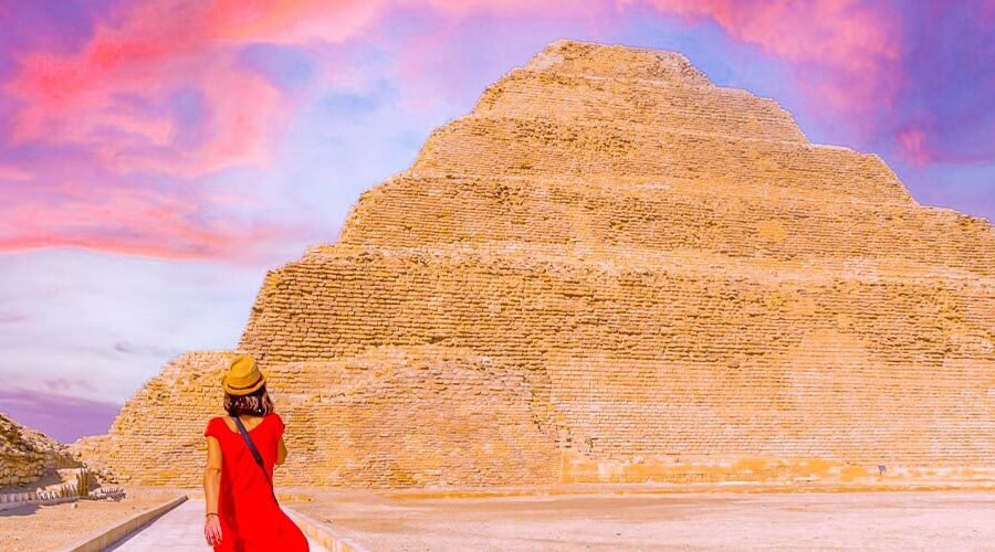 Turista con vestido rojo frente a la pirámide de Zoser al atardecer.