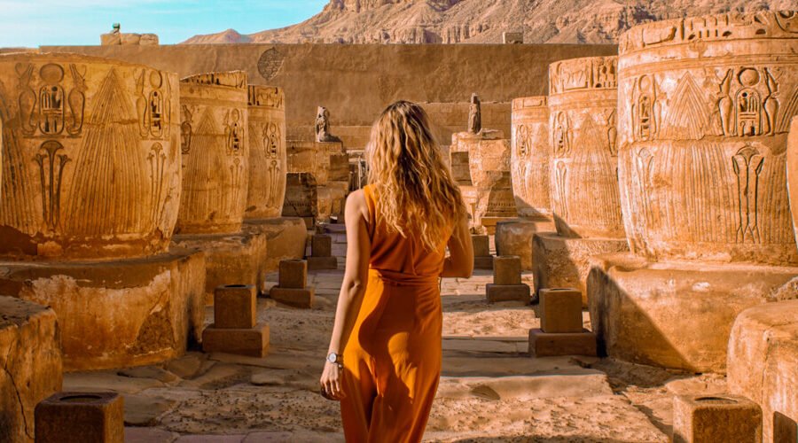 Turista extranjero junto a columnas de templo egipcio en un paisaje impresionante.