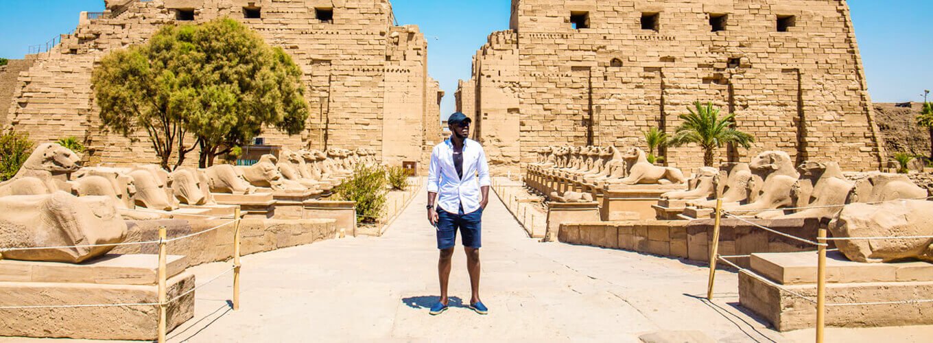 Grandes-fotografías-de-un-hombre-en-el-templo-de-Karnak. Hombre de pie en el Templo de Karnak, destacando la arquitectura antigua y majestuosa.