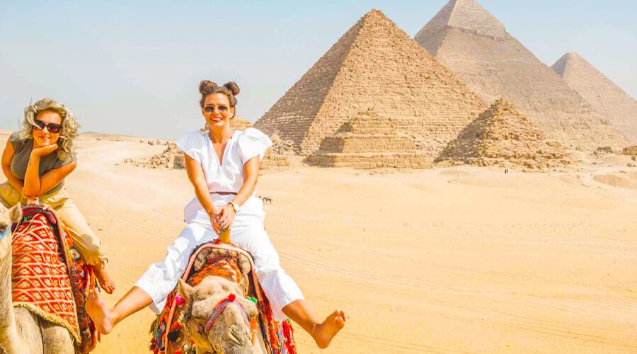Dos niñas montando un camello frente a las pirámides de Egipto.