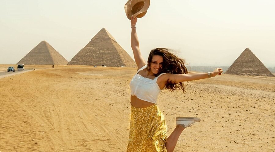 Turista extranjera saltando alegremente frente a las pirámides de Egipto.
