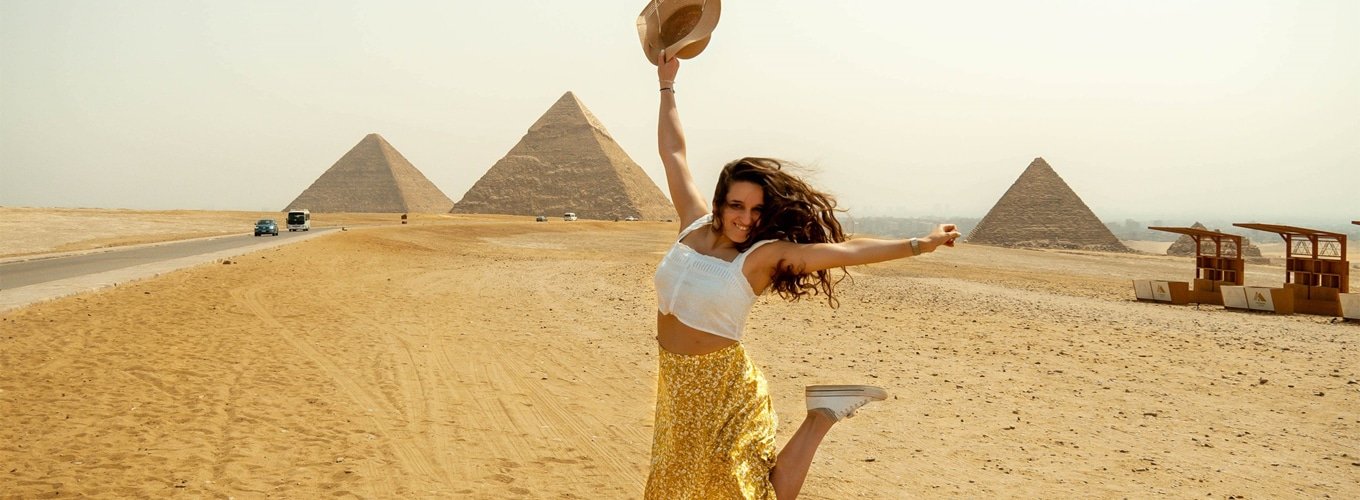 Una-turista-extranjera-se-fotografía-frente-a-las-pirámides-mientras-salta Turista extranjera saltando alegremente frente a las pirámides de Egipto.